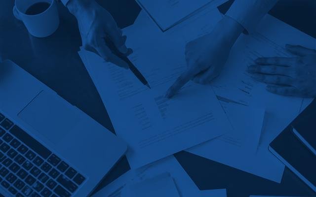 Manos revisando informes de auditoría junto a un notebook
